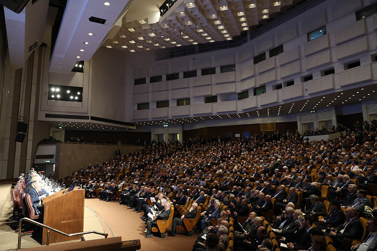 Sala dell'assemblea dei soci del Consorzio Veneto Garanzie con i membri del Consiglio di Amministrazione seduti al tavolo presidenziale, platea di imprenditori e rappresentanti delle imprese consorziate, ambiente istituzionale con bandiere italiana ed europea, atmosfera formale e professionale